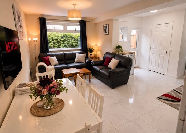 A modern living room with a sofa, a dining table with chairs, a TV, and a window with curtains. - Cathays 6BR House with Garden, Cardiff (Cardiff)