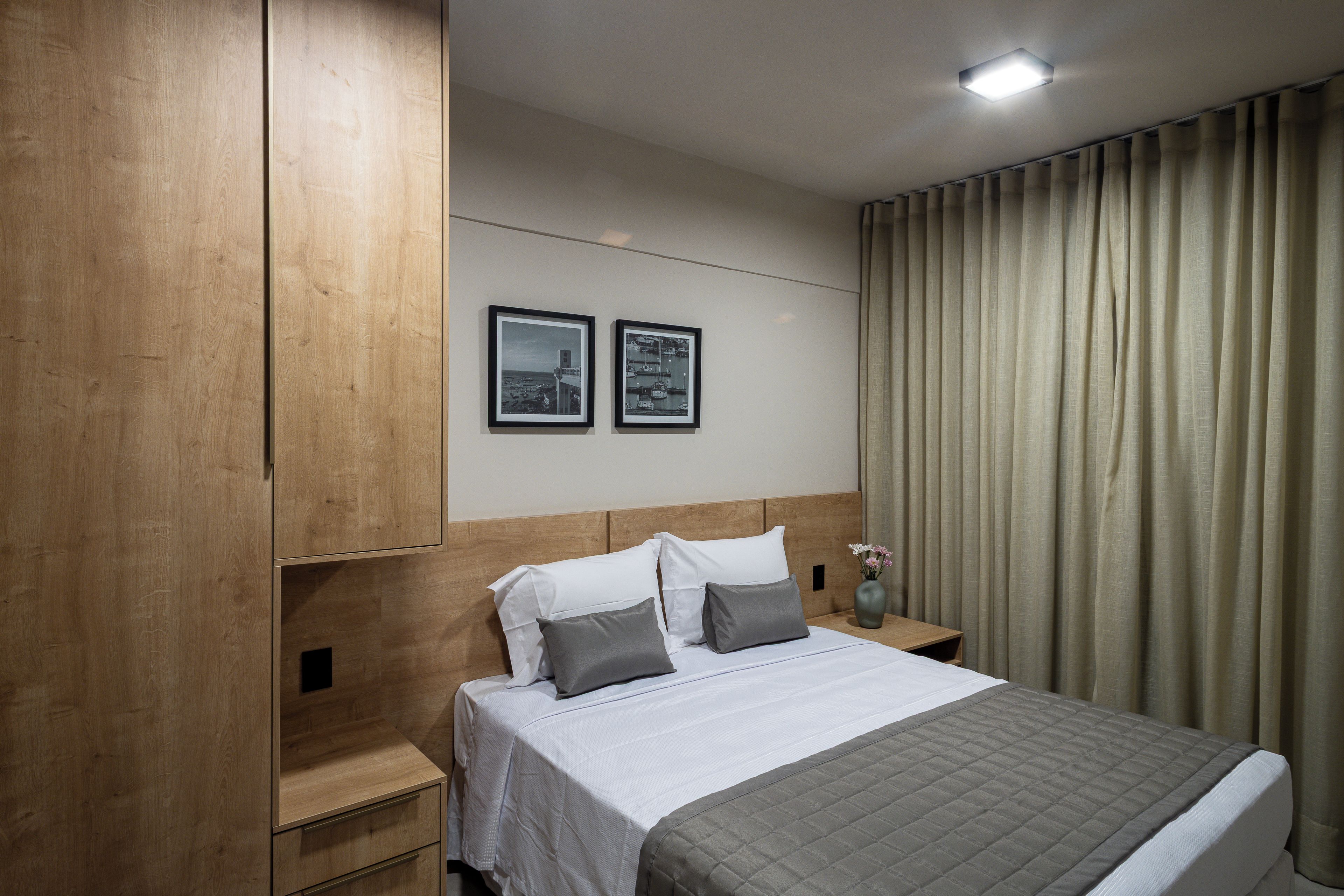 A hotel room with a bed, nightstands, a wooden wardrobe, and two framed pictures on the wall.