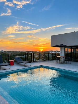 A rooftop pool with a sunset view, lounge chairs, and a table with umbrellas. - Praia do Flamengo Suítes (Salvador)