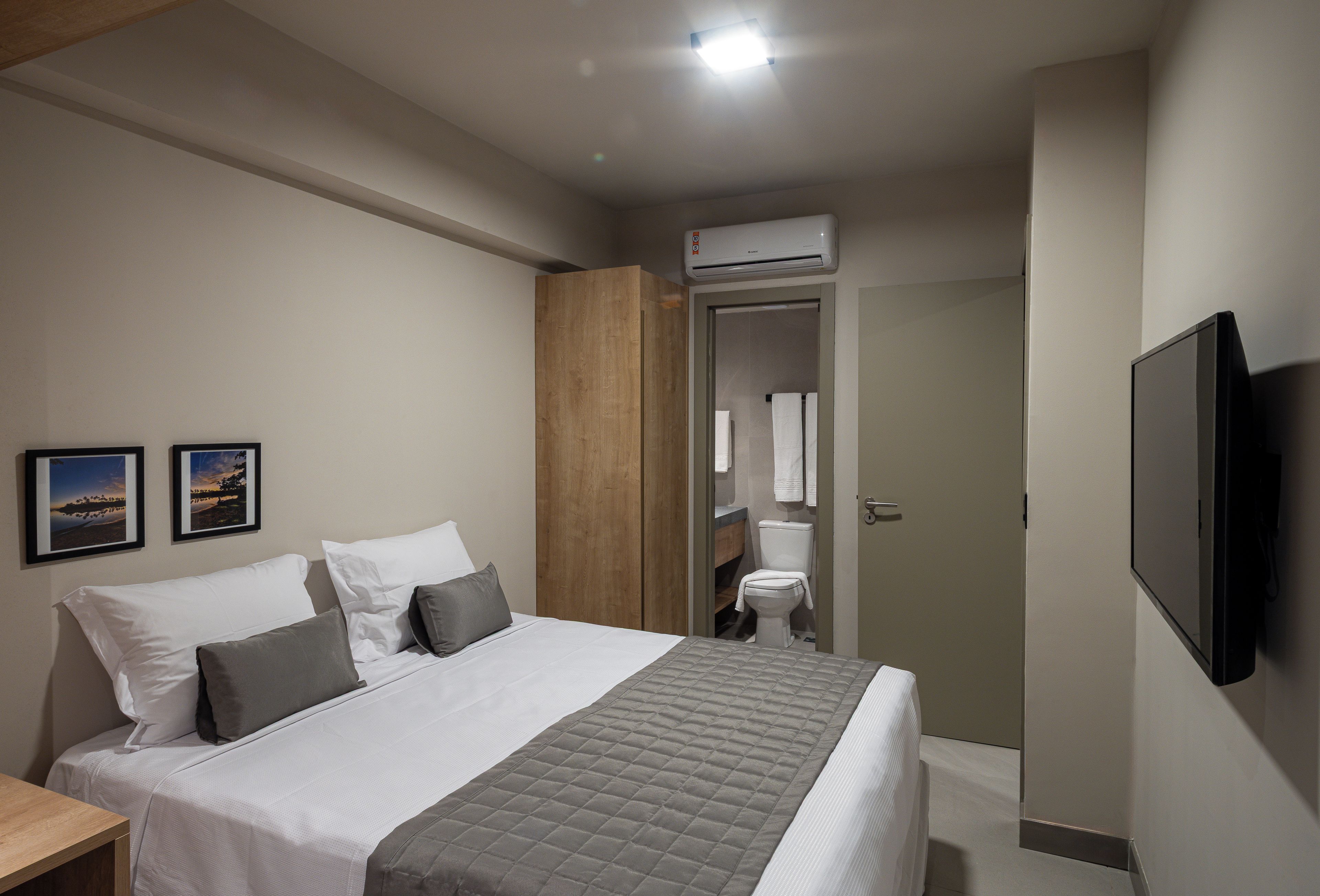 Habitación de hotel con cama, televisión de pantalla plana, armario de madera, inodoro y zona de ducha.