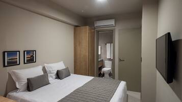 Habitación de hotel con cama, televisión de pantalla plana, armario de madera, inodoro y zona de ducha.