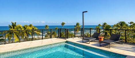 A swimming pool with a view of the ocean, palm trees, and lounge chairs.
