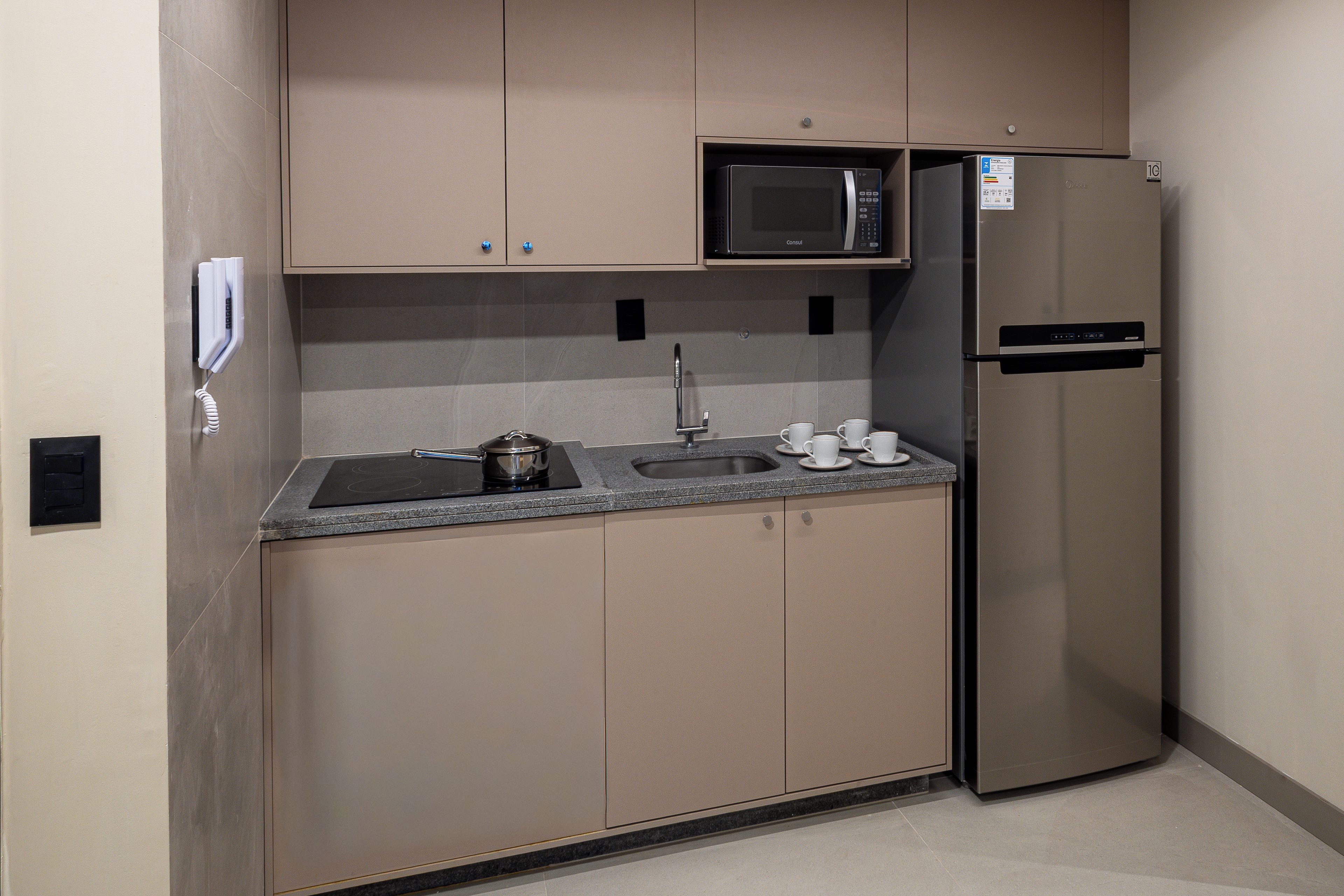 A compact kitchen with a built-in microwave, a stainless steel refrigerator, a sink with a faucet, and a coffee maker.