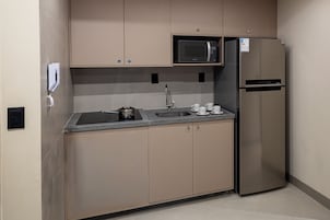 Cozinha compacta com micro-ondas embutido, geladeira de aço inoxidável, pia com torneira e cafeteira.