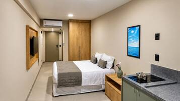 Una habitación de hotel moderna con una cama, un televisor de pantalla plana, un cuadro, una zona de cocina con estufa y un armario de madera.