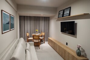 A modern living room with a sofa, dining table, chairs, a TV, and a console table with a vase.