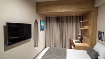 A modern hotel room with a flat-screen TV, a bed with a grey quilt, a desk with a laptop, and a large window with curtains.
