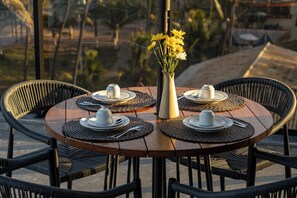 A round wooden table set for four with placemats, white cups, and a vase with yellow flowers.