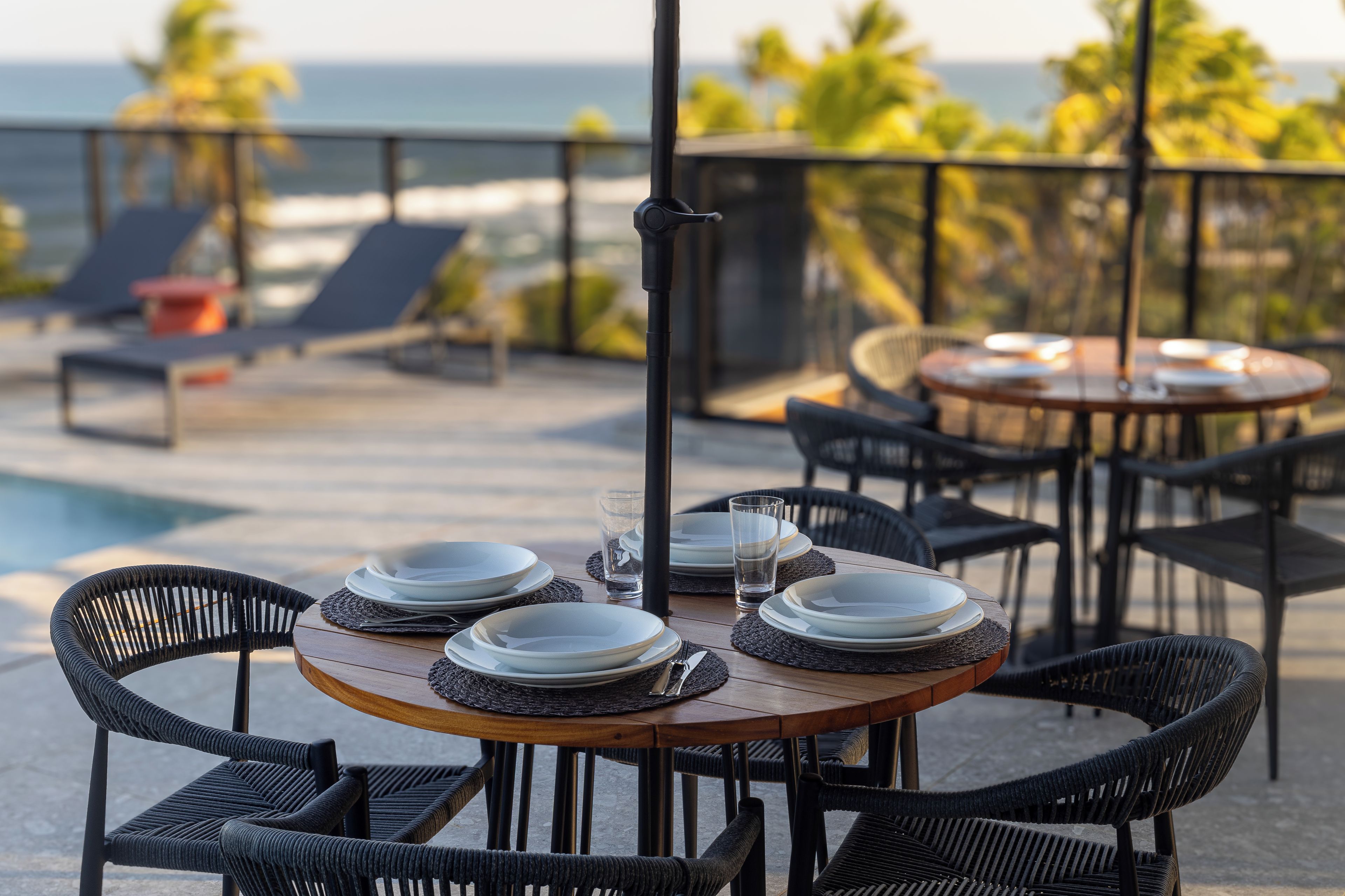 Mesa lista para comer, con sillas, con vista a una piscina y al mar.