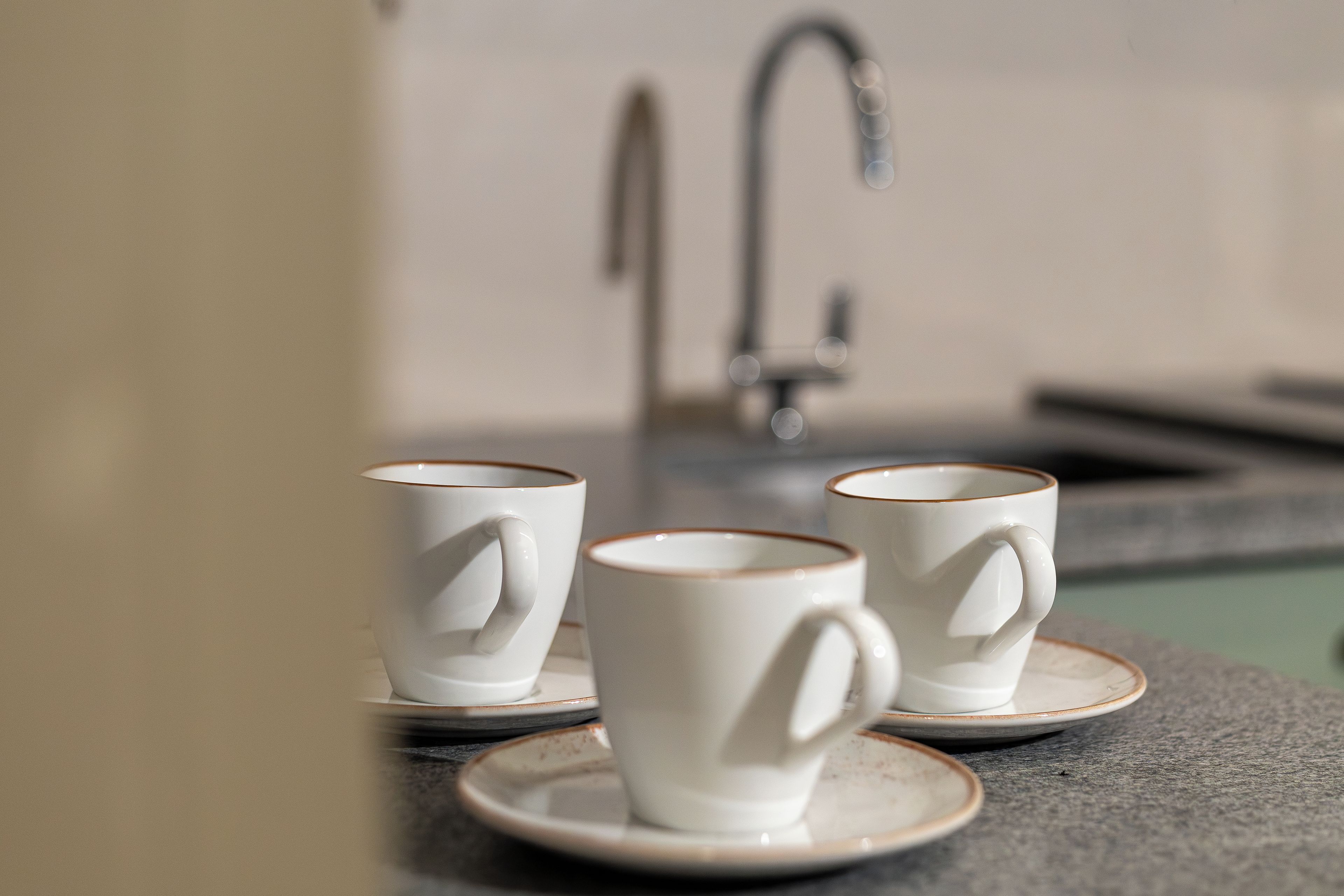 Three white ceramic cups with handles on a matching saucer, placed on a countertop.