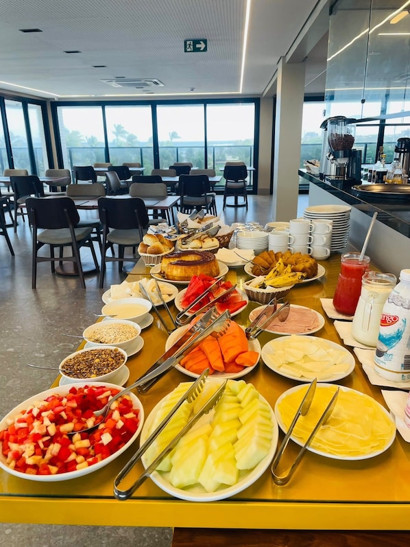 A buffet table with various food items and utensils, a coffee station, and a view of the outdoors through large windows.