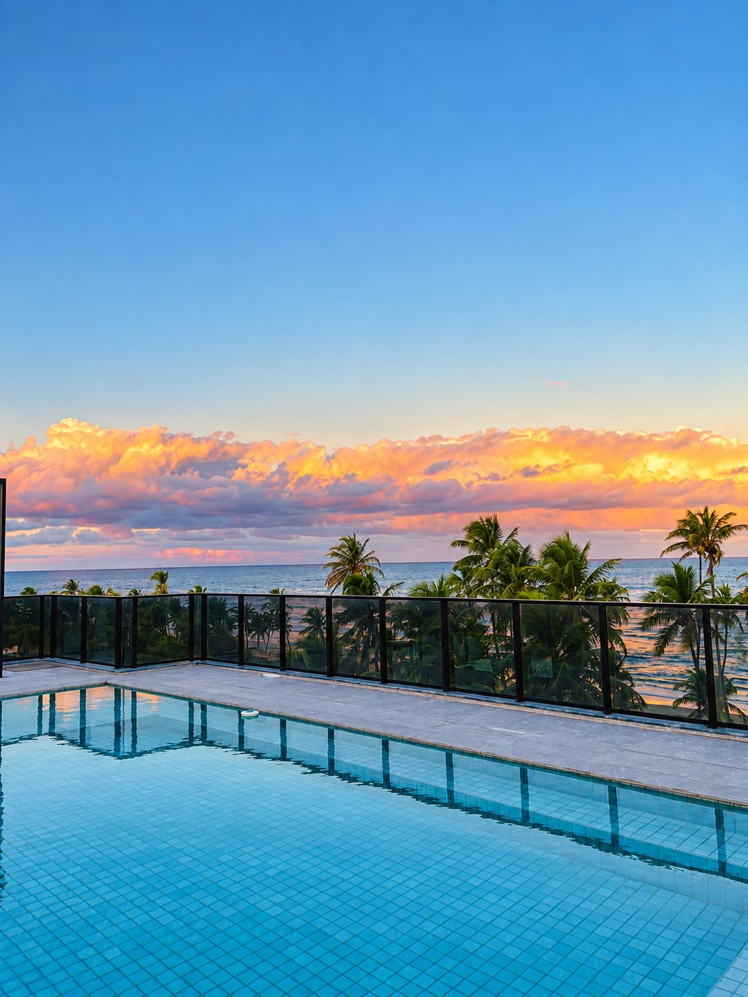 Una piscina con vista al océano y palmeras al atardecer.