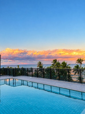 A swimming pool with a view of the ocean and palm trees at sunset.