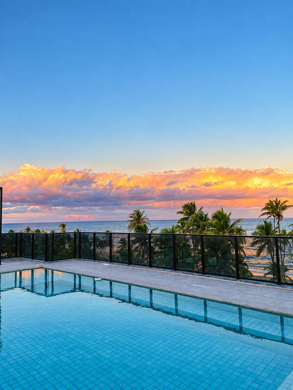 A swimming pool with a view of the ocean and palm trees at sunset.