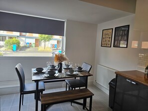 Un coin repas avec une table dressée pour deux personnes, un banc et une vue sur la rue par une fenêtre.