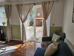 Habitación con sofá, ventana con cortinas, radiador y vista a un edificio de ladrillo.