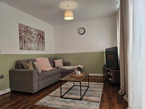Un salon avec un canapé gris, une table basse, une horloge et un téléviseur.