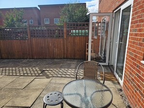 Une terrasse avec une table et des chaises, une clôture en bois et un mur en briques.