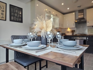 Un comedor moderno con una larga mesa dispuesta para cuatro, con platos grises, tazones y copas de vino transparentes.