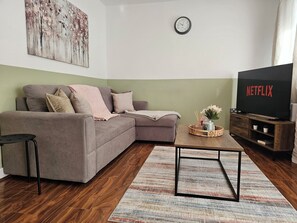 Una sala de estar con sofá, mesa de centro, televisor y un reloj en la pared.