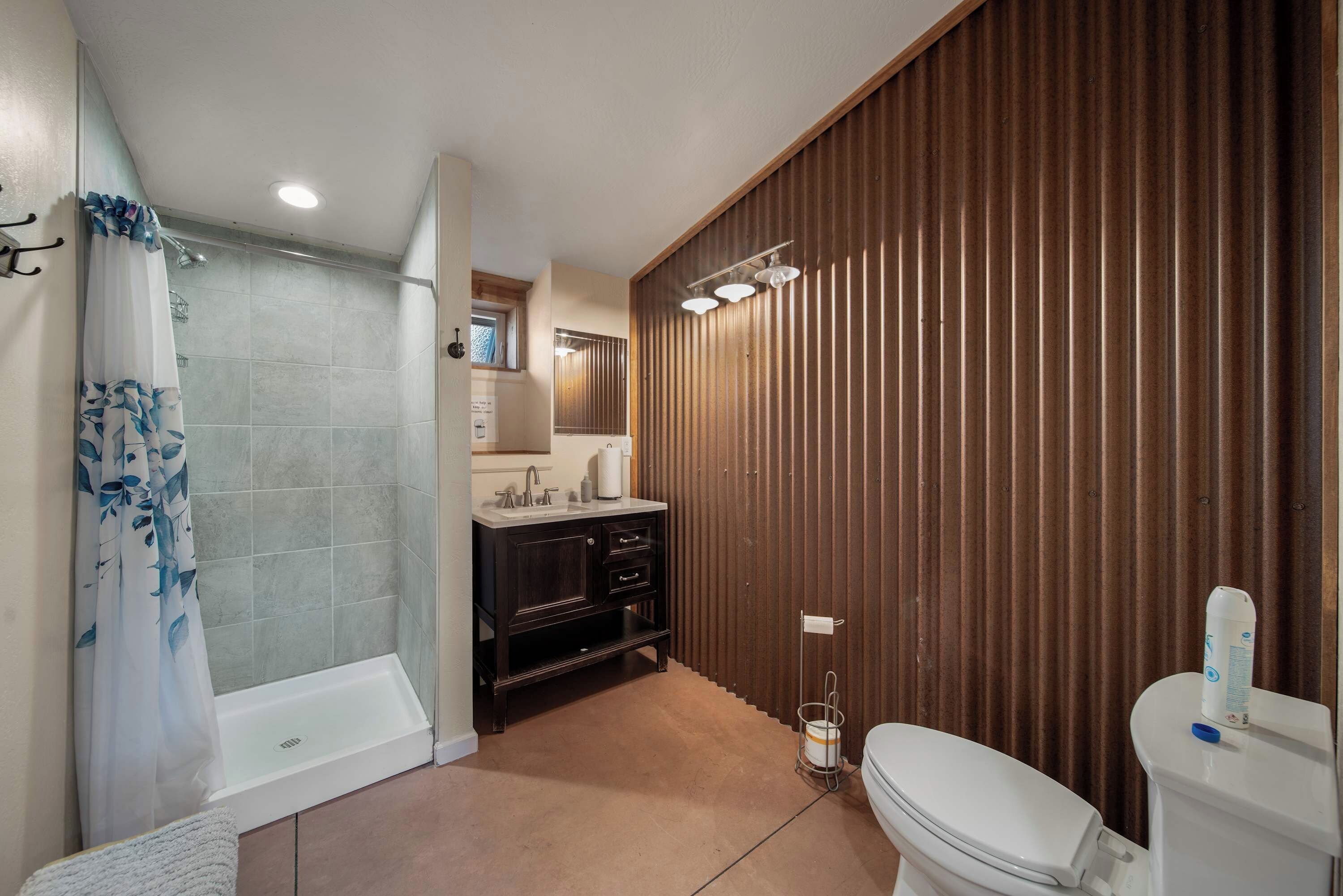 A bathroom with a shower, toilet, sink, and wooden paneling.