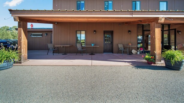 A two-story building with a covered patio area, outdoor seating, and potted plants.