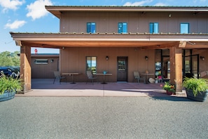 A two-story building with a covered patio area, outdoor seating, and potted plants.