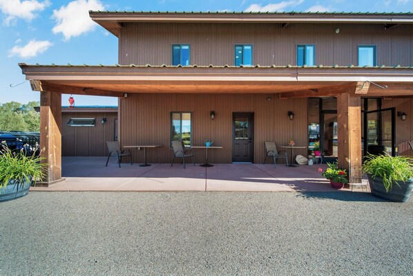 A two-story building with a covered patio area, outdoor seating, and potted plants.