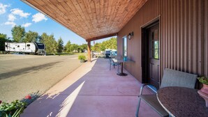 A covered outdoor area with a concrete patio, a table and chairs, and a view of a trailer park in the background.