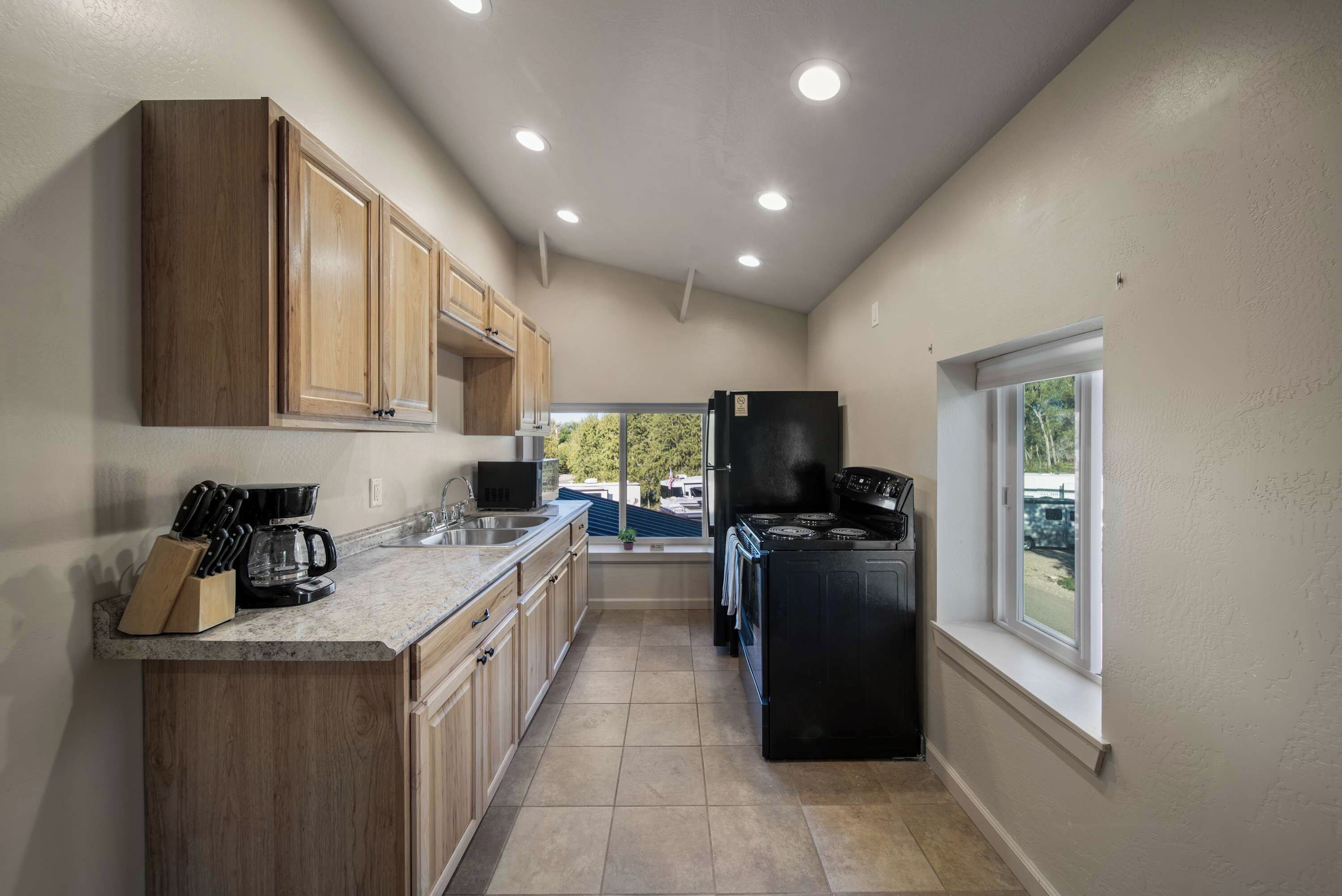 A compact kitchen with wooden cabinets, a black refrigerator, and a window providing a view of the outdoors.