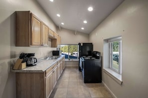 A compact kitchen with wooden cabinets, a black refrigerator, and a window providing a view of the outdoors.