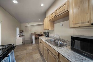 A compact kitchen with wooden cabinets, a stainless steel sink, a microwave, and a dining area with chairs and a table.