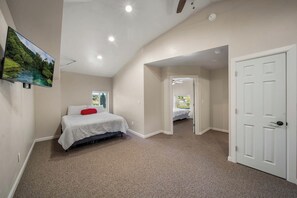 A bedroom with a bed, a door, and a view of a garden through a window.