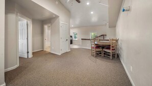 A spacious room with a ceiling fan, a dining table with chairs, and a kitchen area in the background.