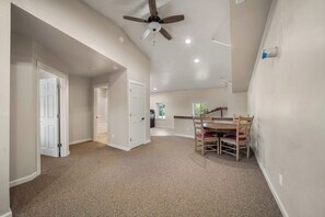 A spacious room with a ceiling fan, a dining table with chairs, and a kitchen area in the background.