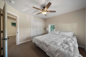 A bedroom with a bed, a ceiling fan, a door, and a window.