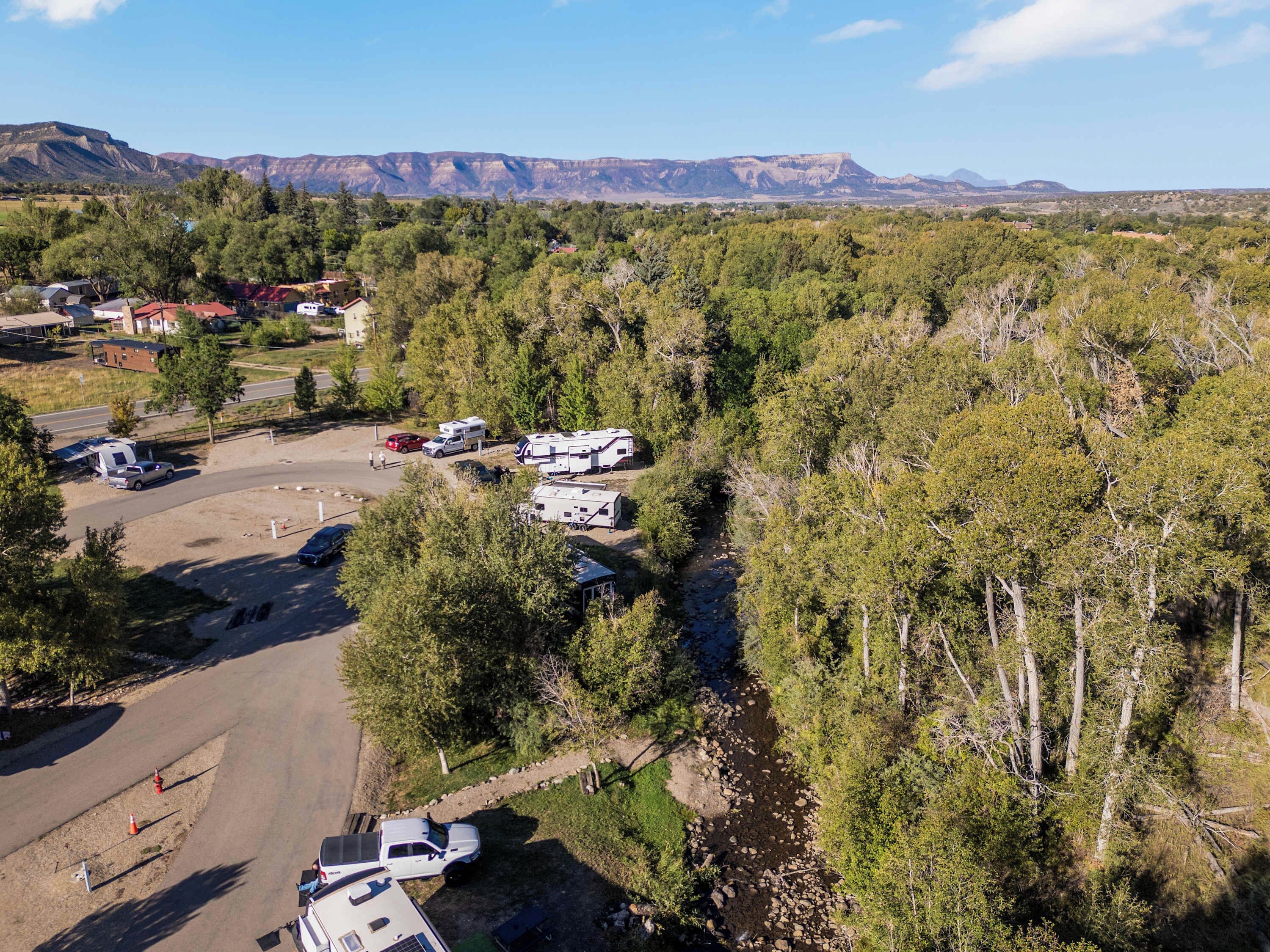Ein Campingplatz mit Reisemobilen und Autos, umgeben von Bäumen und Bergen im Hintergrund.
