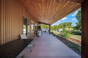 An outdoor patio area with a wooden ceiling, a table and chairs, and a view of a parking lot and trees.