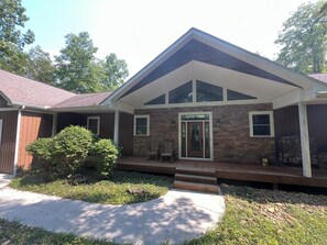 A two-story house with a stone facade, a front porch with chairs, and a small garden area. - 4Bdrm Lakefront on Quiet Cove. Gradual slope from road to water. (Jacksboro)