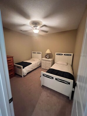 A bedroom with two single beds, a nightstand with a lamp, a dresser, and a ceiling fan. - 4Bdrm Lakefront on Quiet Cove. Gradual slope from road to water. (Jacksboro)