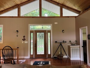 Quarto com teto de madeira, um telescópio sobre um tripé, porta com vitrais e uma cadeira.