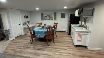 A dining area with a wooden table and chairs, a kitchen with a microwave and sink, and a hallway with a door.