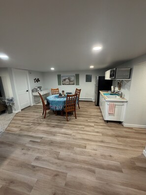 A dining area with a wooden table and chairs, a kitchen with a microwave and sink, and a hallway with a door.