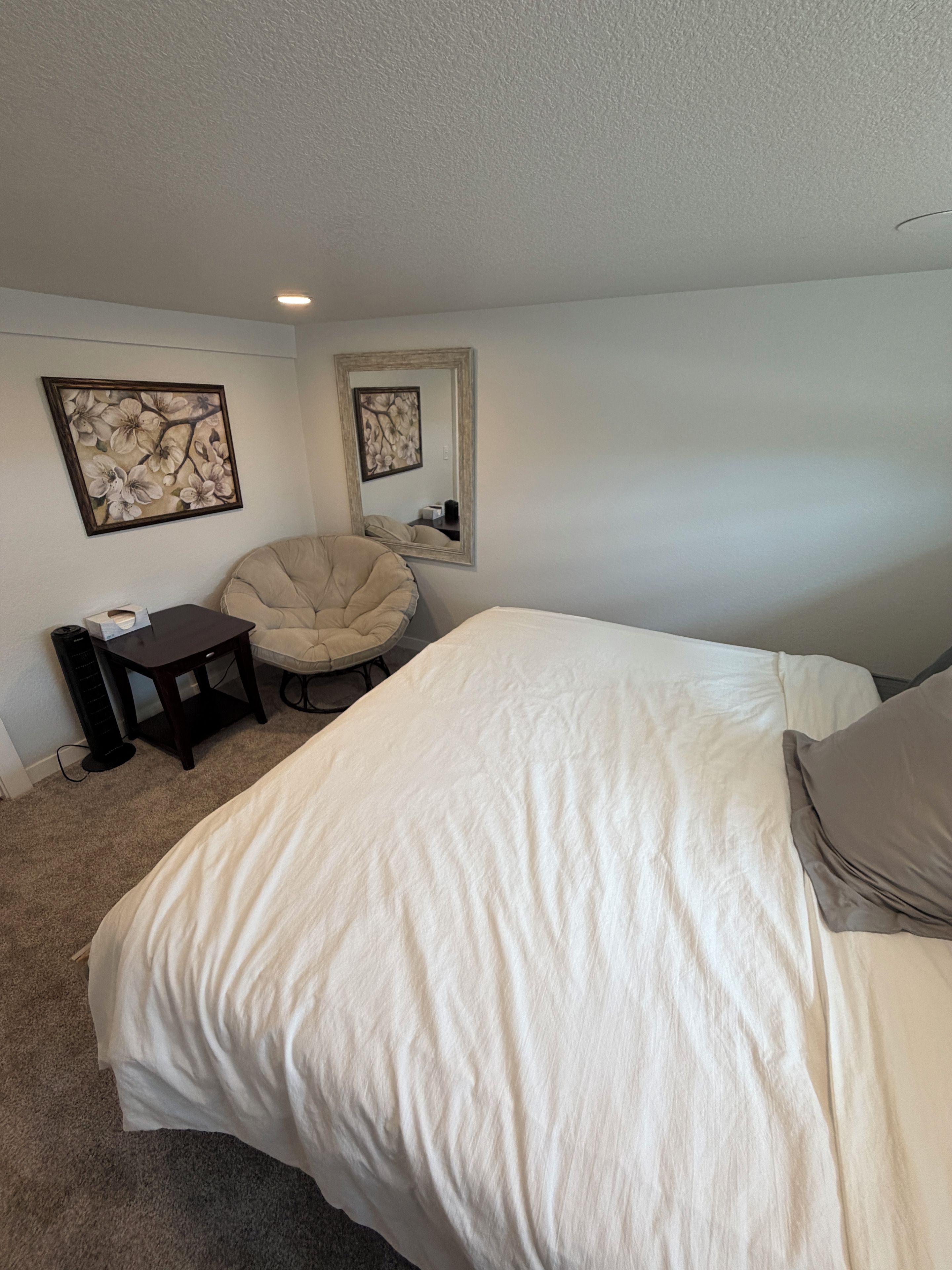 A bedroom with a large bed, a chair, a small table, and two wall-mounted mirrors.