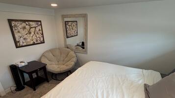 A bedroom with a large bed, a chair, a small table, and two wall-mounted mirrors.