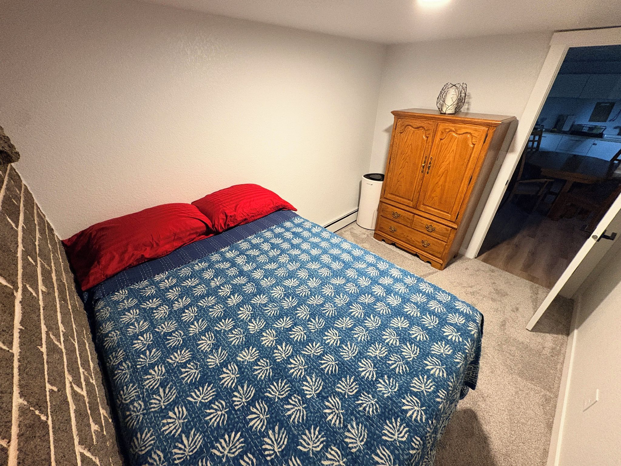 A bedroom with a bed, a wooden wardrobe, and a door leading to a hallway.
