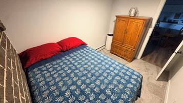 A bedroom with a bed, a wooden wardrobe, and a door leading to a hallway.