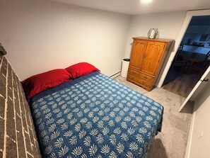 Une chambre à coucher avec un lit, une armoire en bois et une porte donnant sur un couloir.