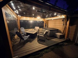 An outdoor deck with wooden flooring, a hot tub, and seating area with chairs and a table.