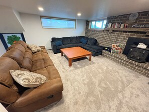 A living room with a brown sofa, a wooden coffee table, a dark grey sectional sofa, and a brick fireplace.